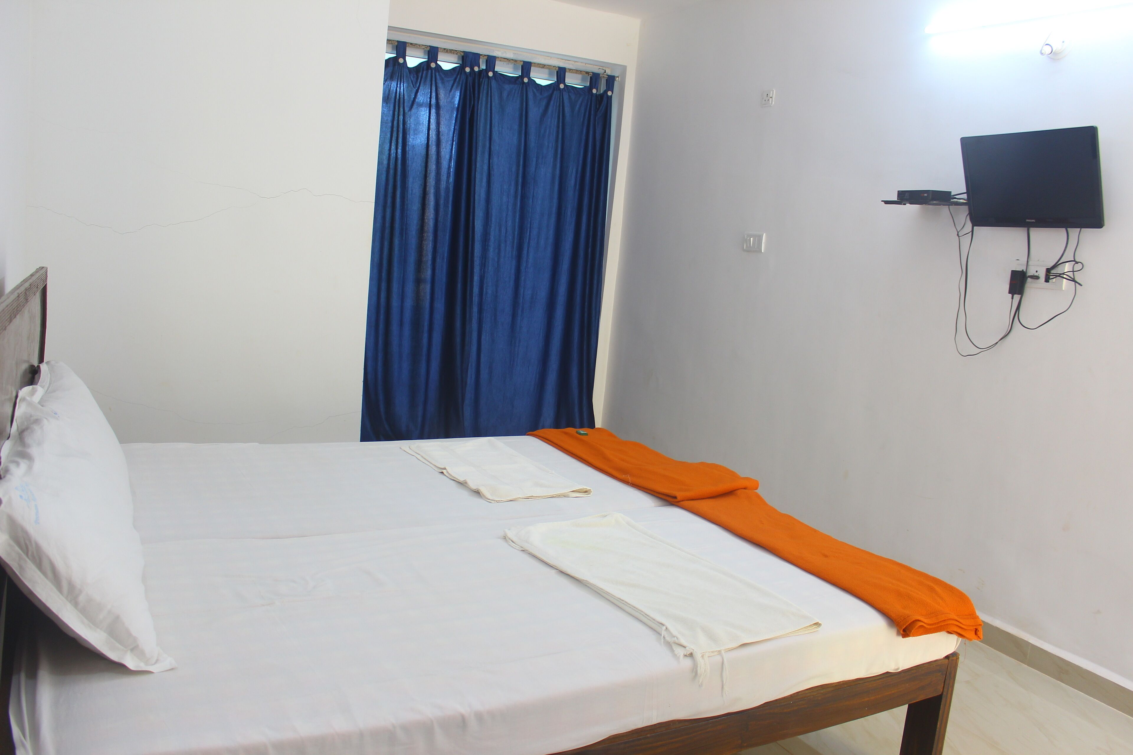 A bedroom with a bed, a television mounted on the wall, and a window with blue curtains.