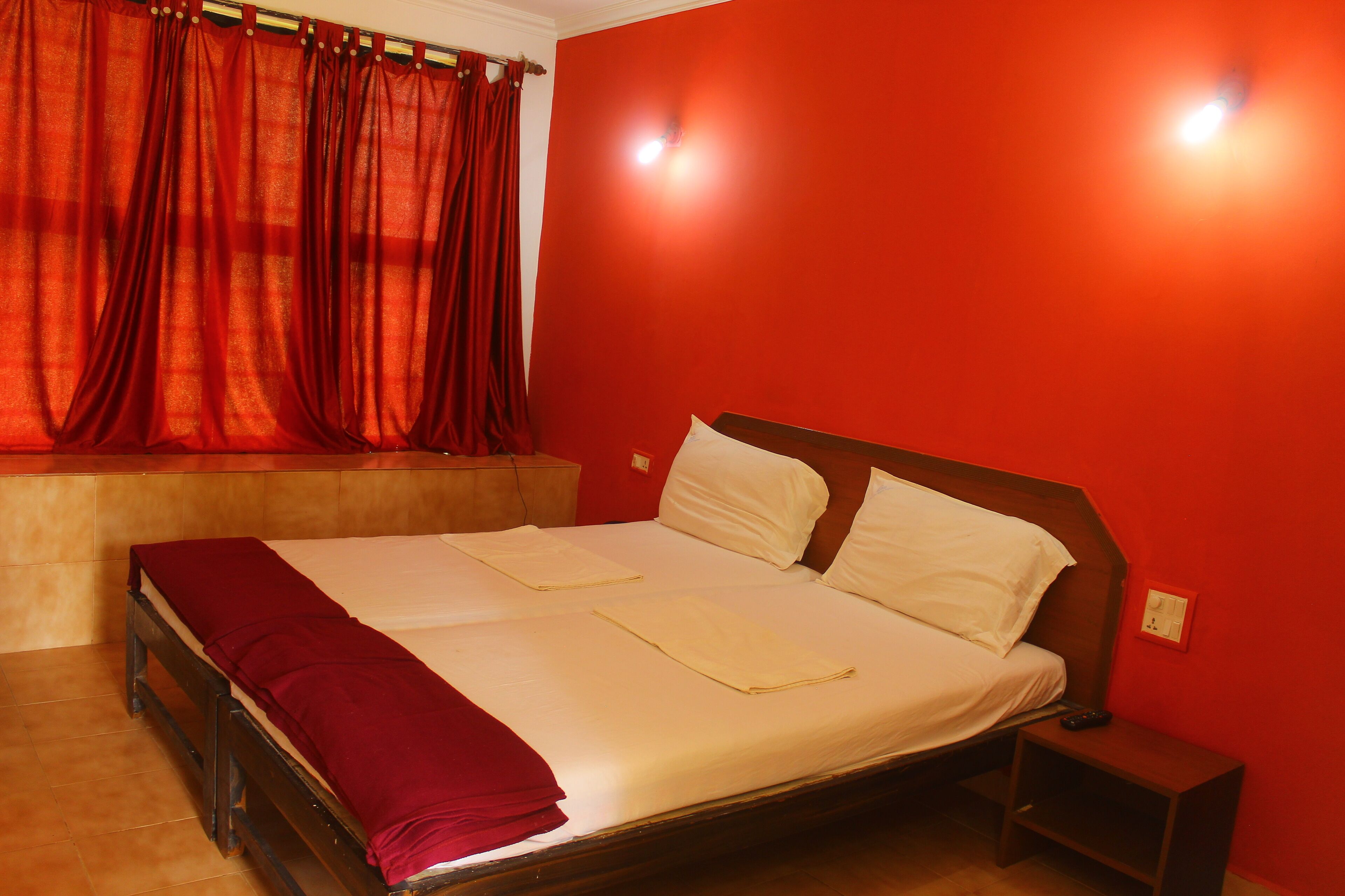 A bed with white linens, a wooden headboard, and a red curtain.