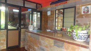Un área de recepción con una pared de azulejos, un mostrador de recepción, una planta en maceta y un cuadro en la pared.