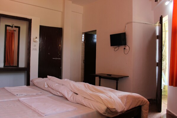A bedroom with a bed, a TV mounted on the wall, and a door leading to another room.