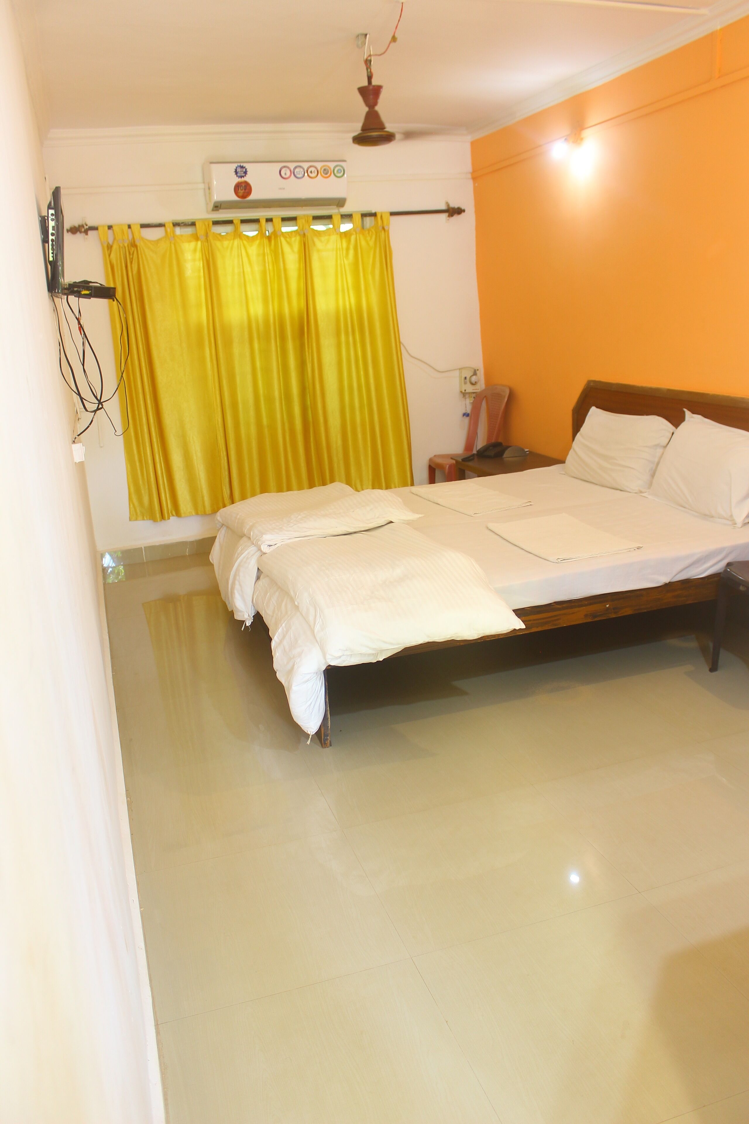 A bedroom with a bed, a ceiling fan, an air conditioner, and a yellow curtain.