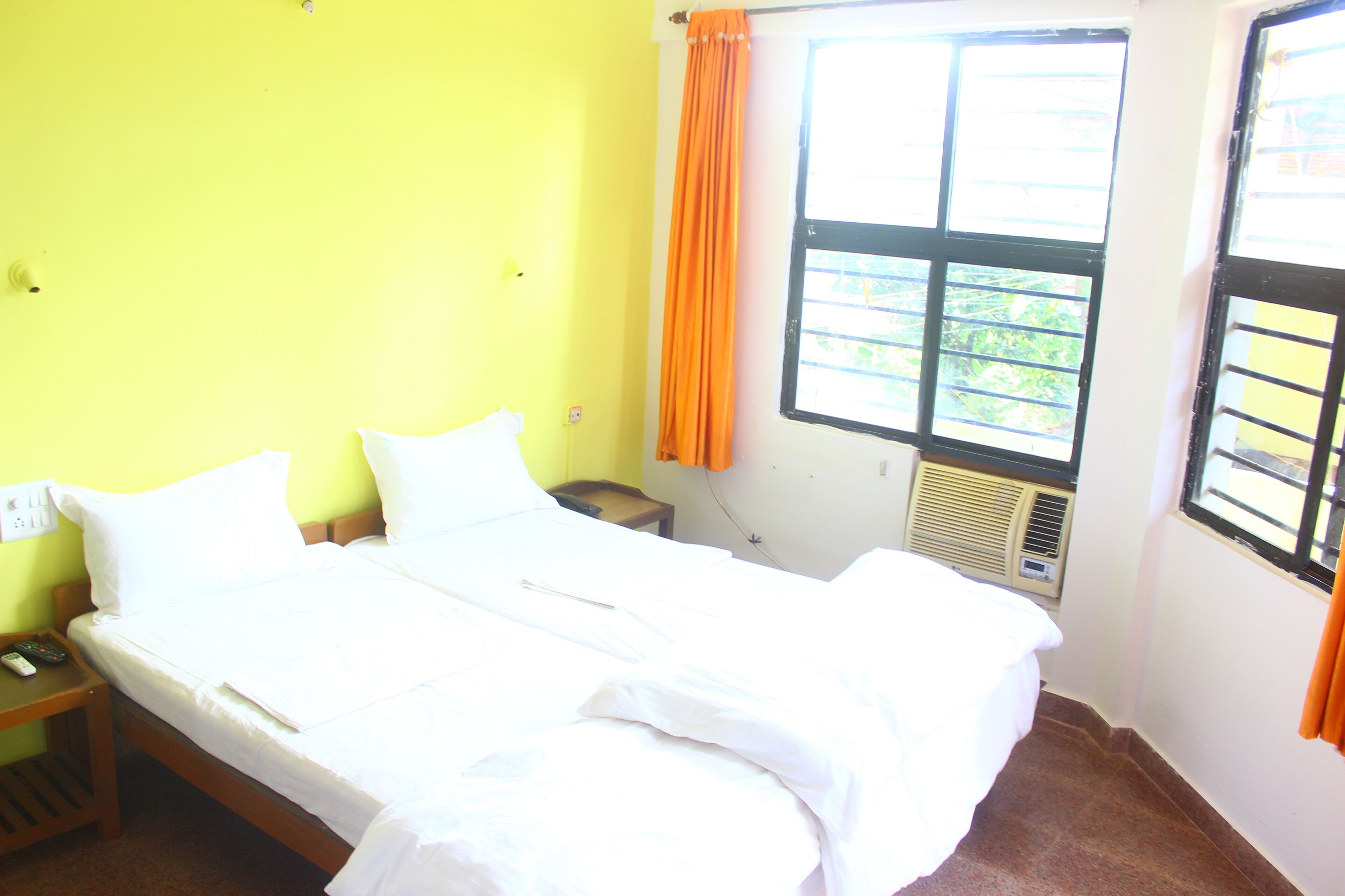 A room with a bed, a nightstand, a window with curtains, and a wall-mounted air conditioning unit.