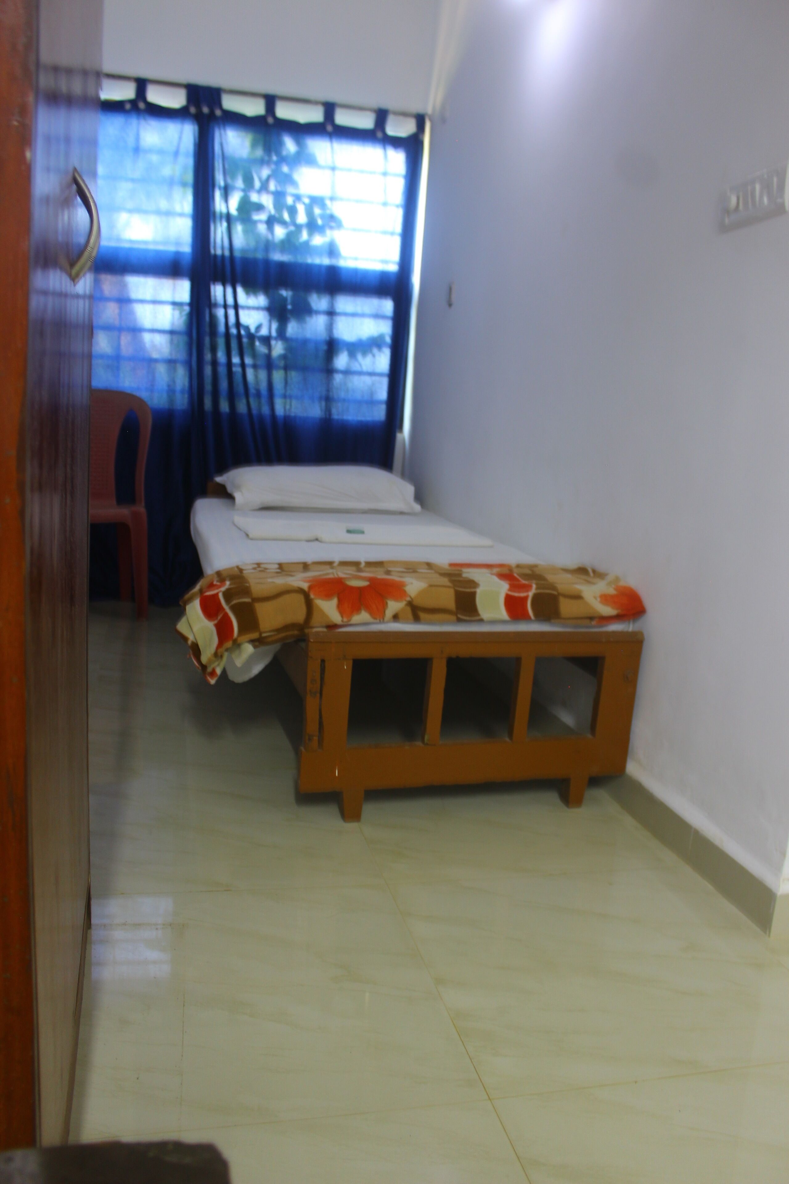 Ein Zimmer mit einem Bett, einer hölzernen Bank, einem roten Stuhl und einem Fenster mit Vorhängen.