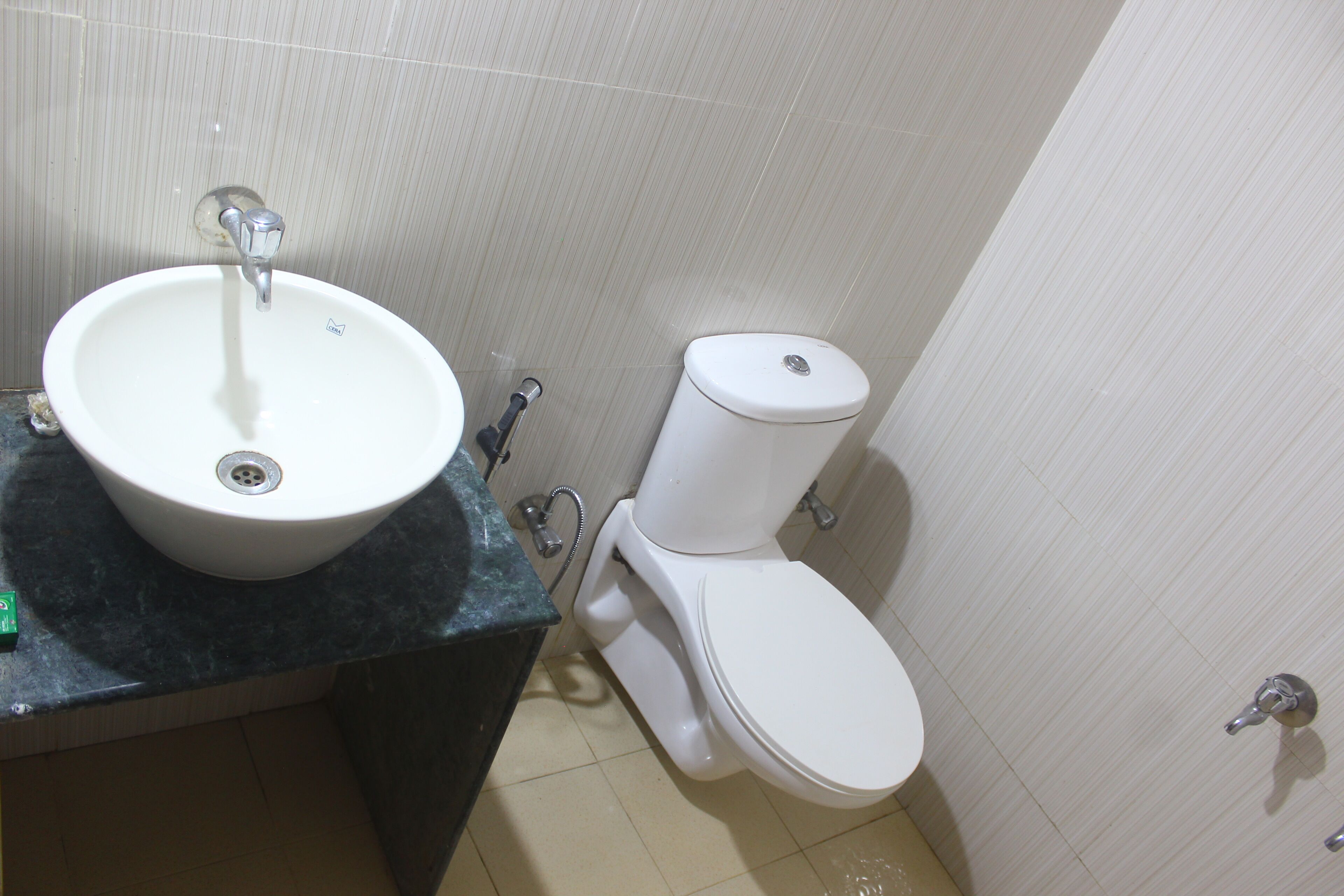 Un baño con lavamanos, inodoro y cabezal de ducha blancos.