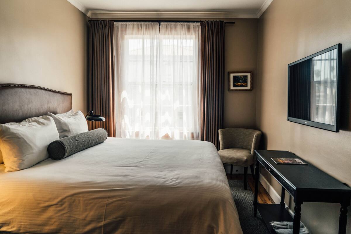 A hotel room with a large bed, a desk, a chair, and a television.