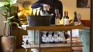 Un espace bar avec un barman préparant des boissons, un chariot à bouteilles de vin et un sol à carreaux.