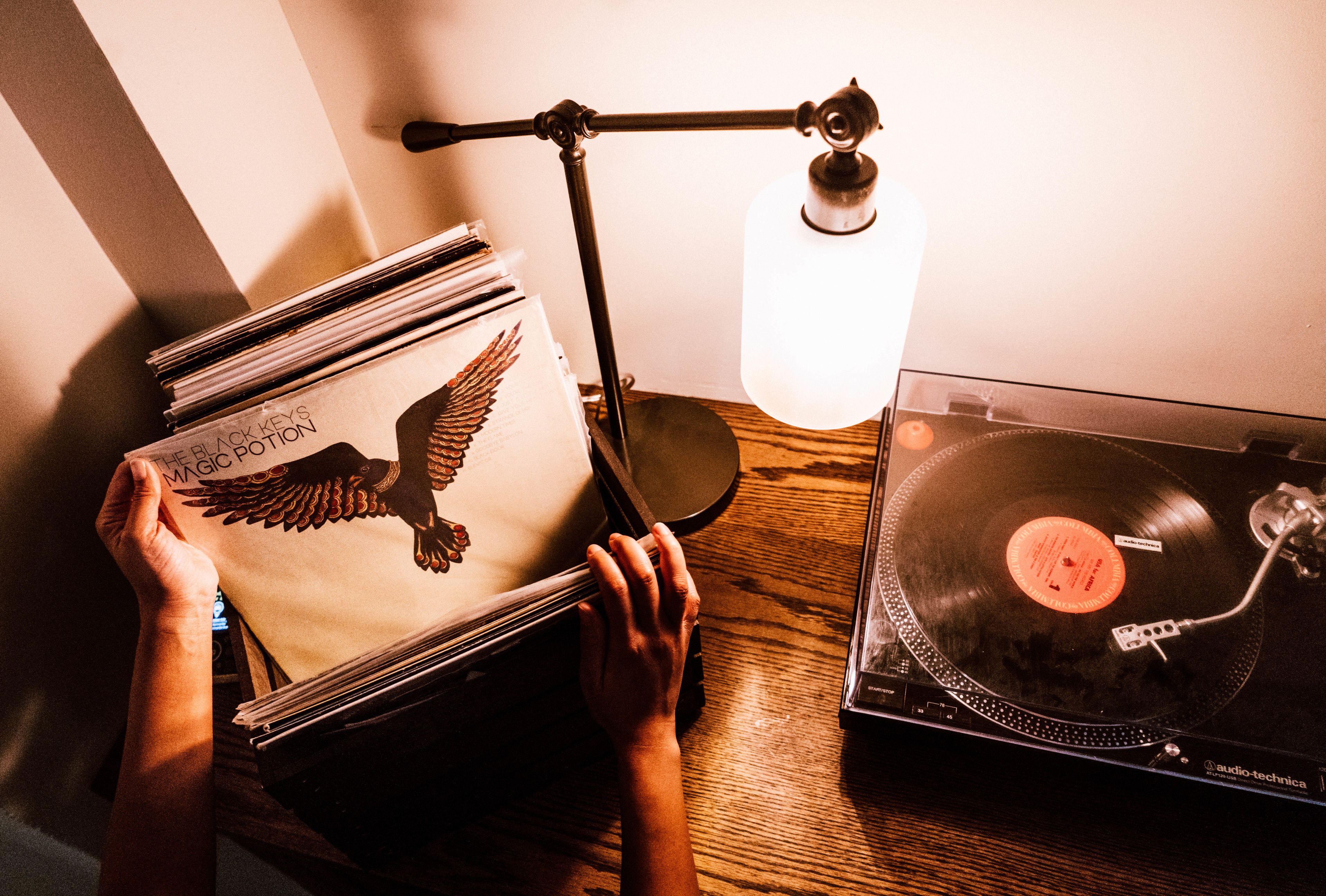A person holding a stack of vinyl records next to a turntable on a wooden table.