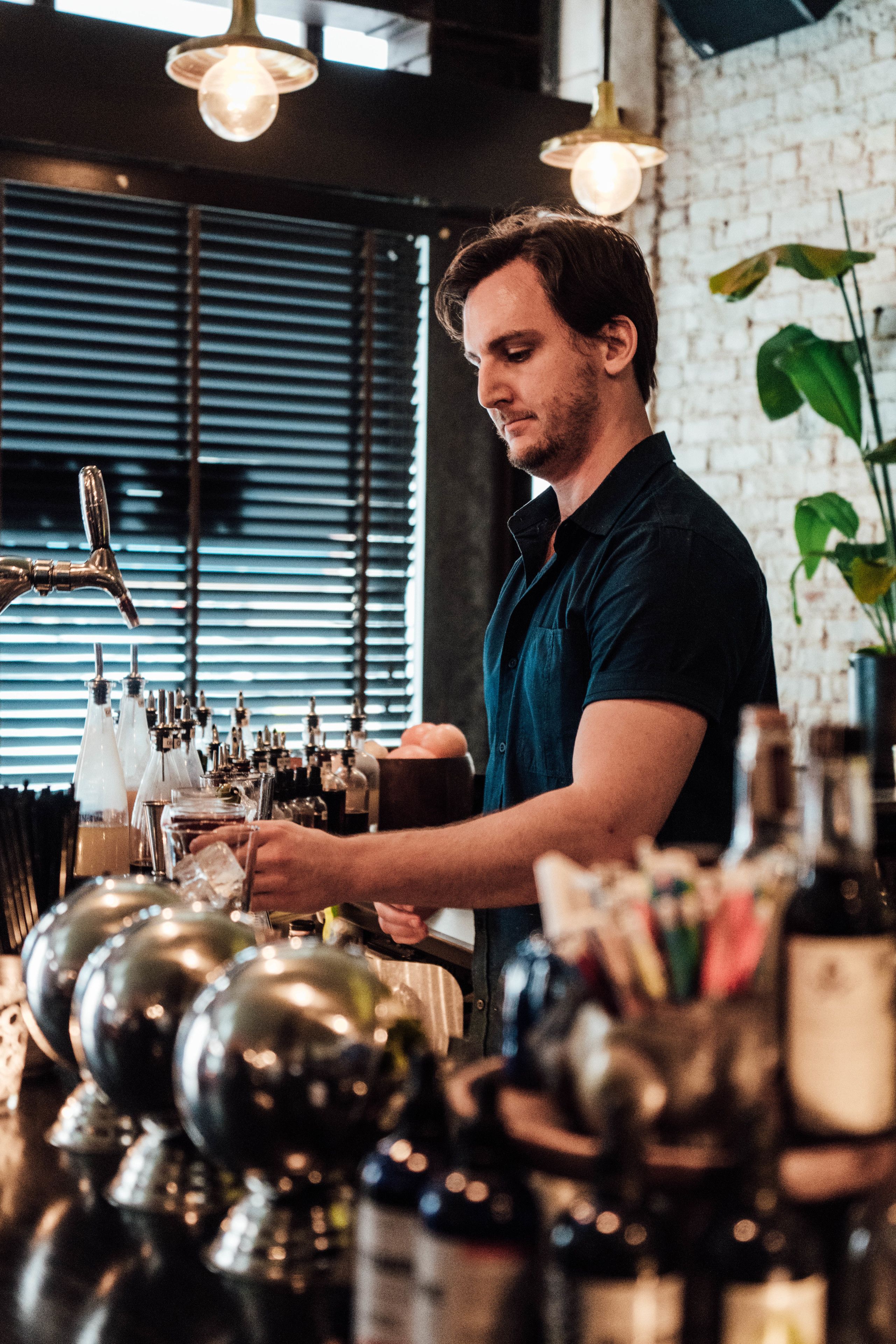 Un barman derrière un comptoir où l’on peut voir une grande variété de bouteilles et de verres.