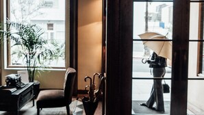 Un hall d’hôtel avec une grande fenêtre en arc de cercle, un fauteuil, une petite table avec un parapluie et un panneau indiquant la sortie.