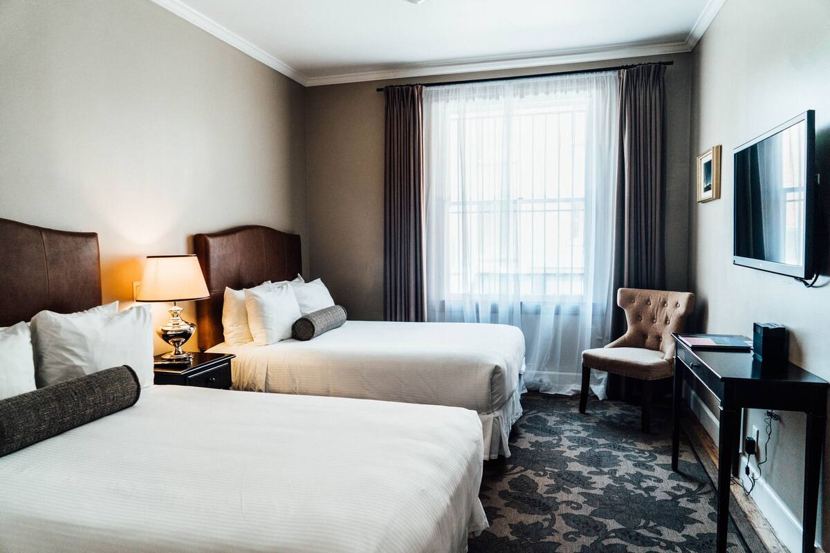 A hotel room with two beds, a desk, a chair, a TV, and a window with curtains.