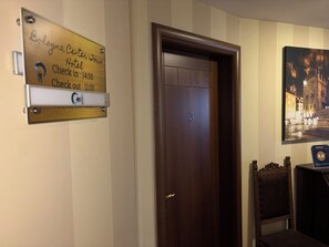 A hotel room with a wooden door, a check-in/out sign, and a framed picture on the wall. - Bologna Center Town (Bologna)
