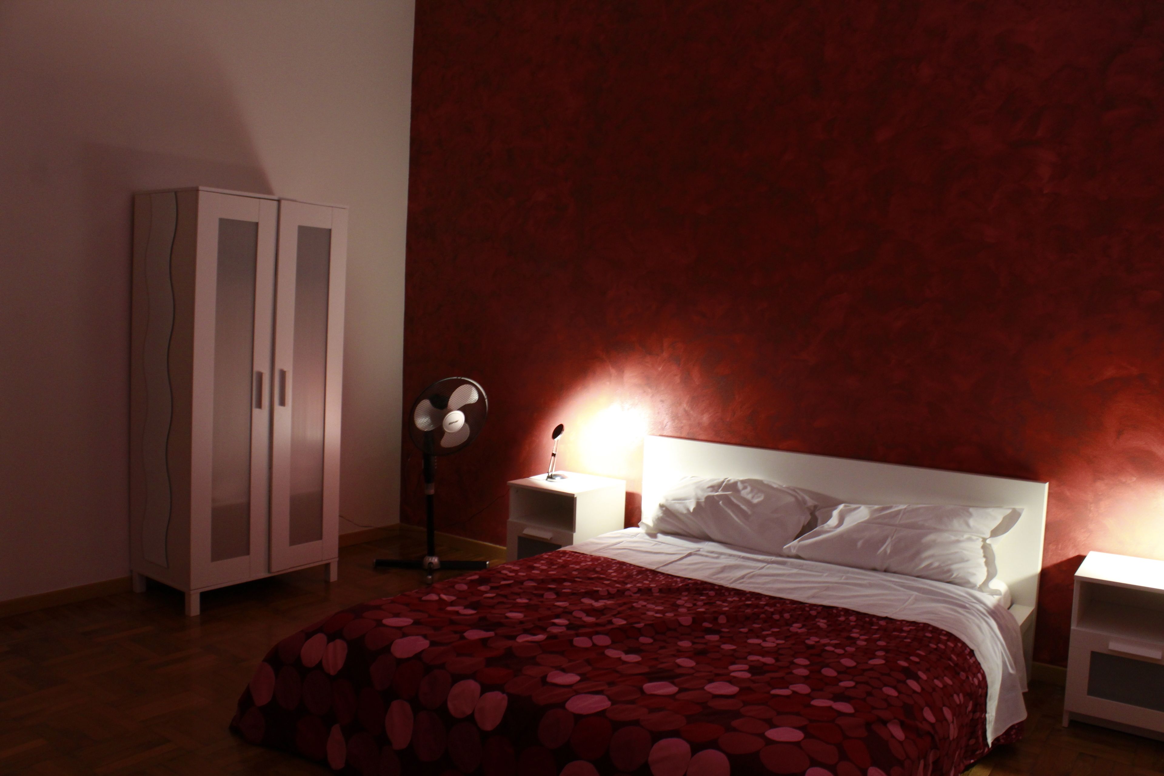 Quarto com cama, guarda-roupa e mesa de cabeceira com abajur.
