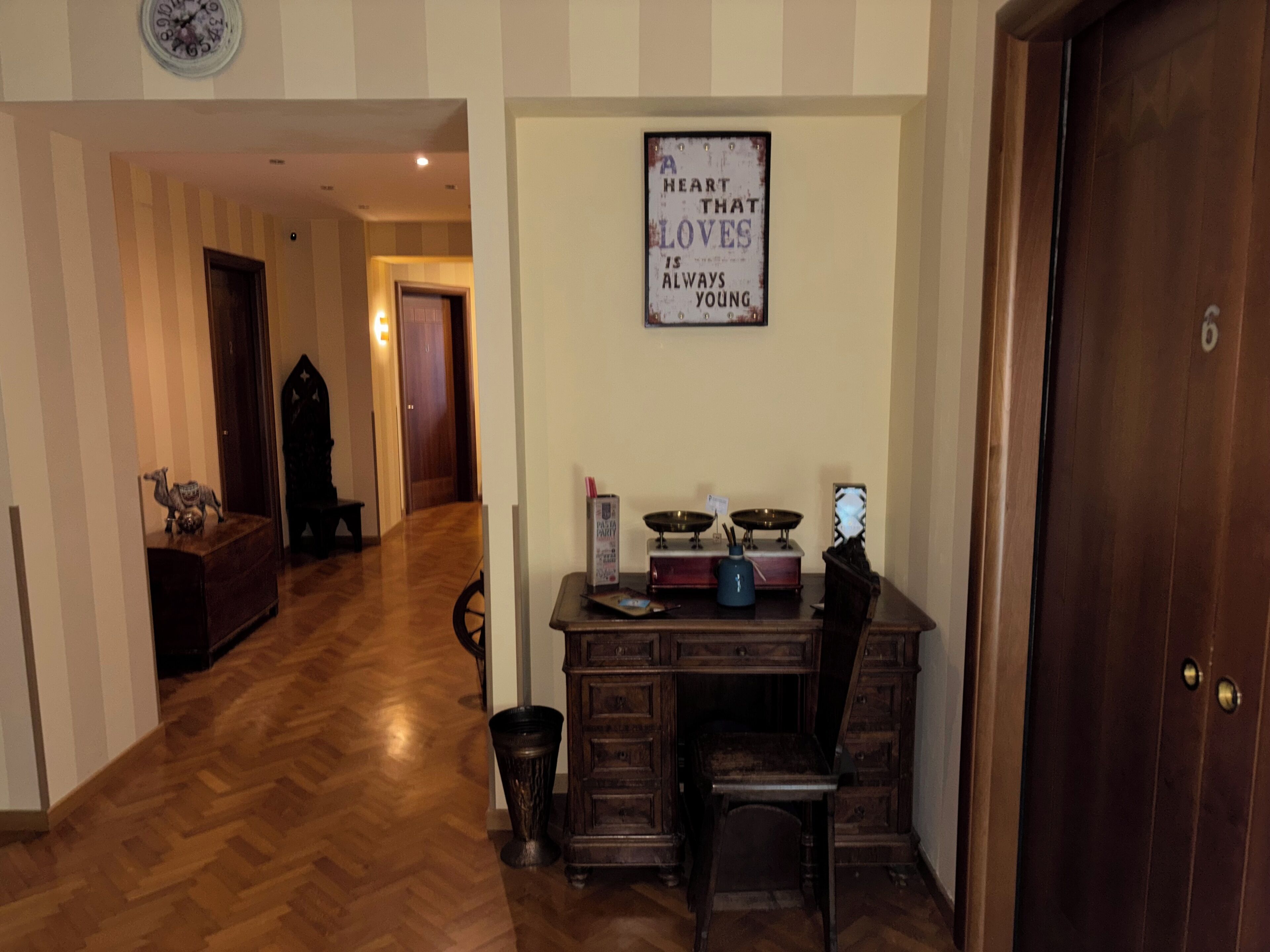 A room with a wooden herringbone floor, a desk with a chair, a clock on the wall, and a framed quote.