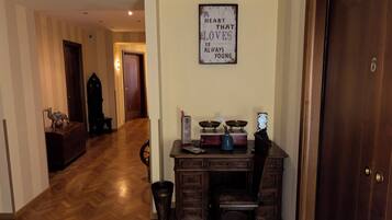 A room with a wooden herringbone floor, a desk with a chair, a clock on the wall, and a framed quote.