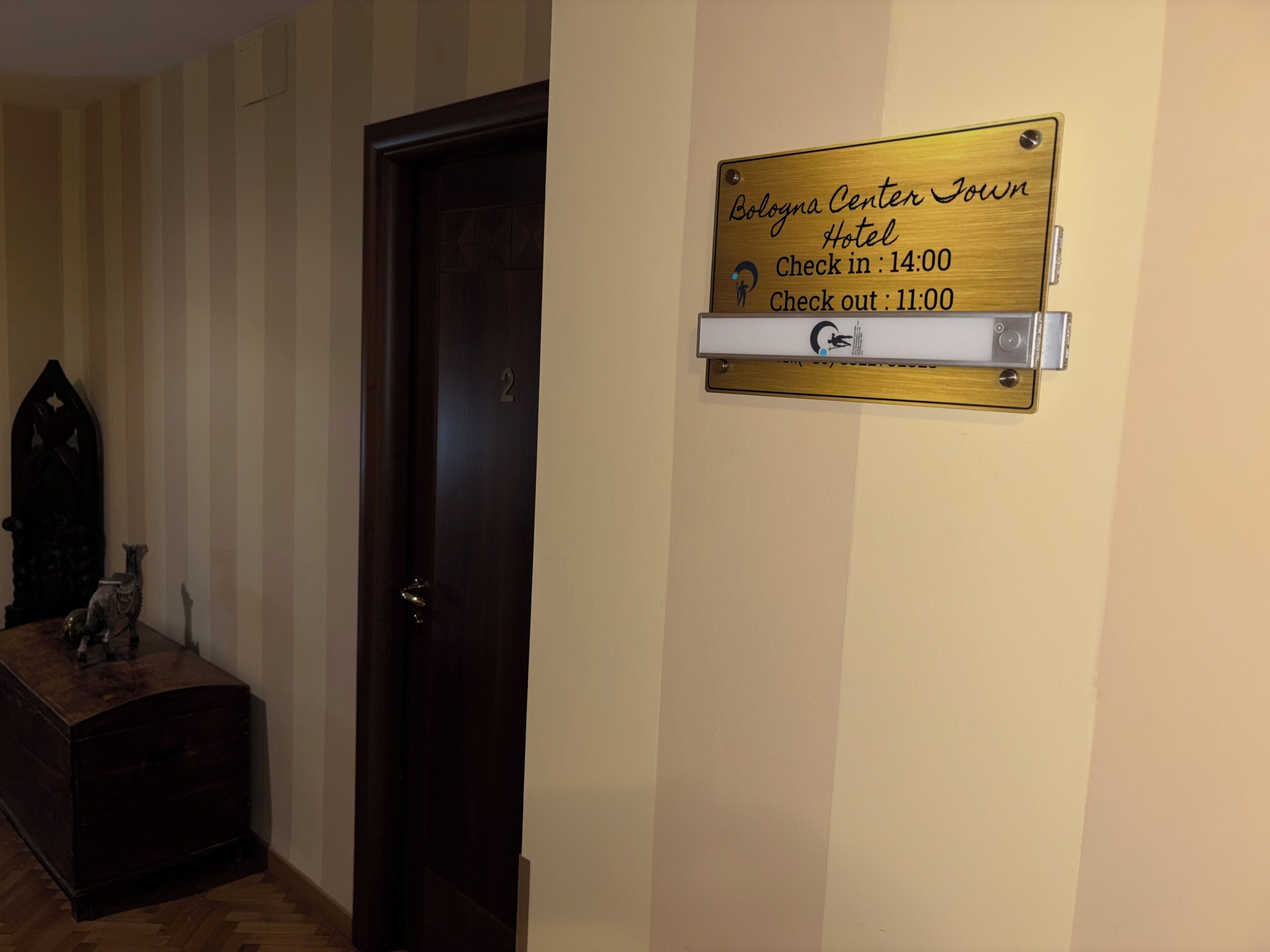 A wooden door with a brass plaque indicating the Bologna Center Town Hotel's check-in and check-out times.