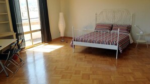 A bedroom with a wooden parquet floor, a white metal bed frame, striped bedding, a standing lamp, and a window with curtains. - Bologna Center Town (Bologna)
