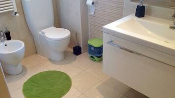 A bathroom with a toilet, bidet, sink, and green rug.