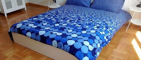 A bed with a blue polka dot bedspread, a white bedside table, and a white lamp.