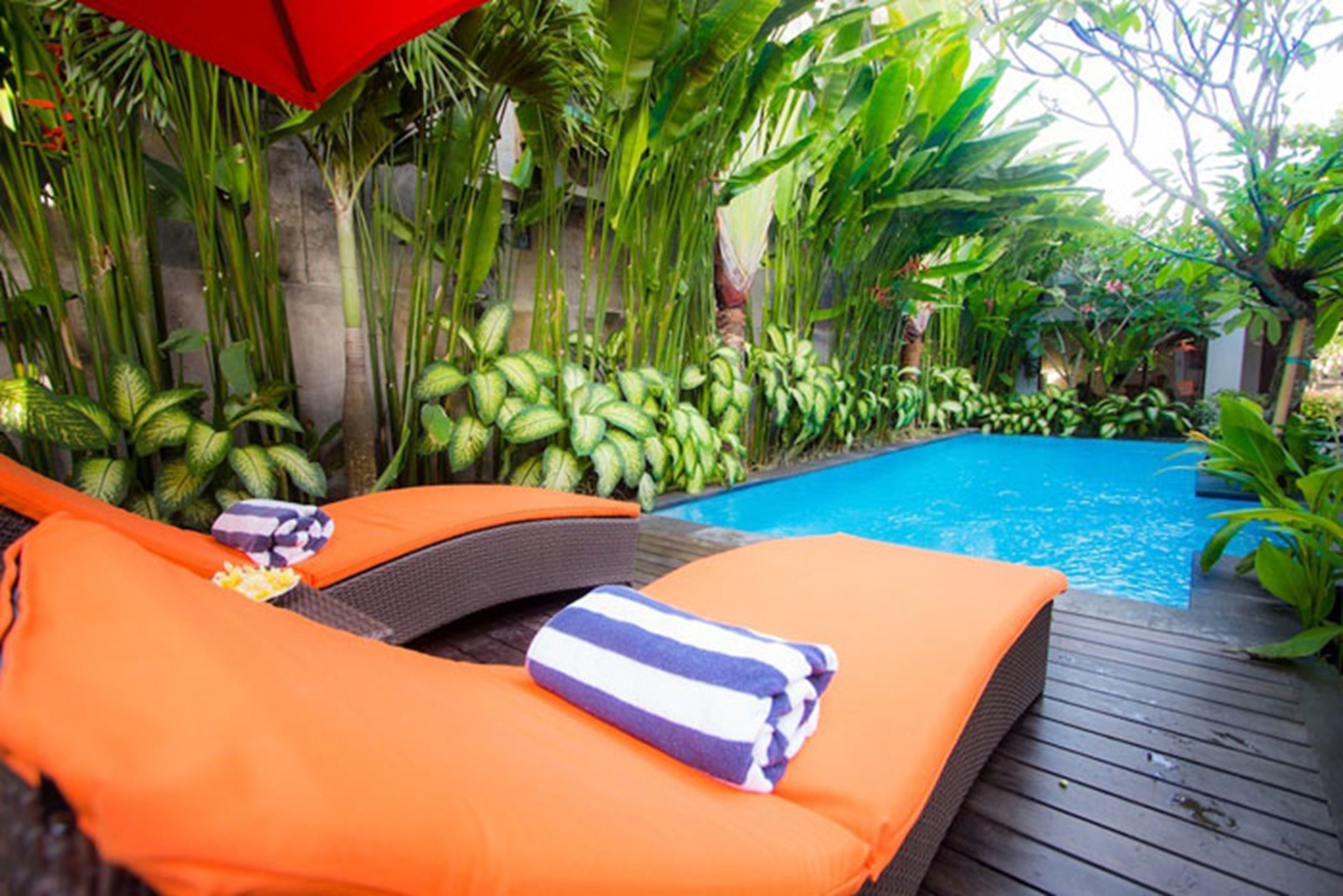 A poolside area with lounge chairs and a red umbrella.