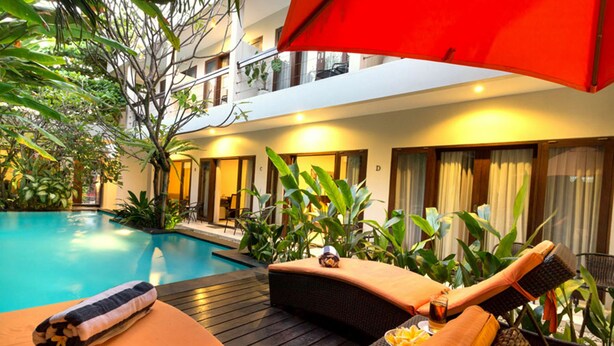 Zona de piscina con sillones reclinables, una sombrilla roja y una terraza de madera.