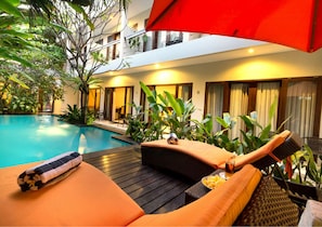 A poolside area with lounge chairs, a red umbrella, and a wooden deck.