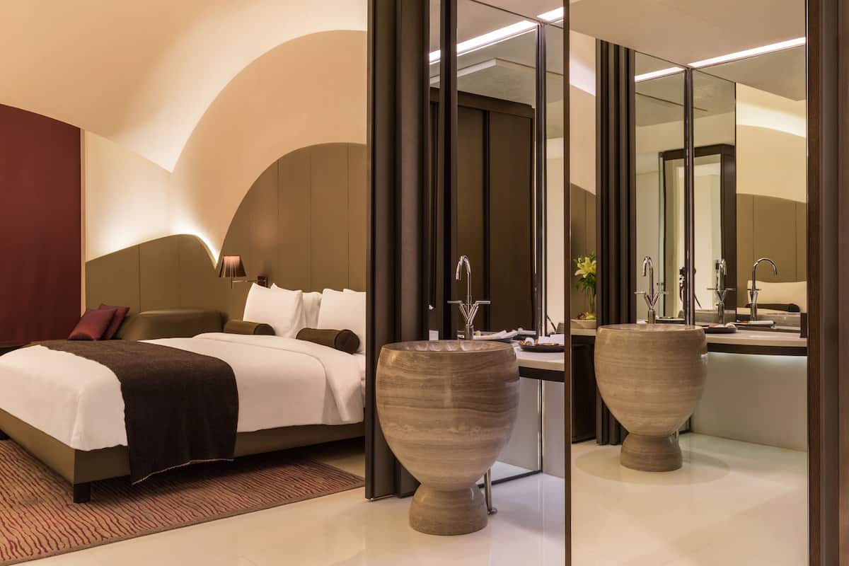 A modern hotel room with a large bed, a vanity with a mirror, and two large vases.