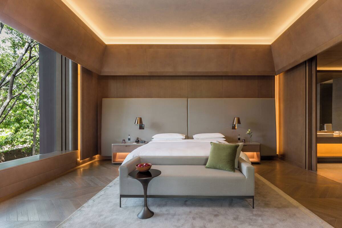 Ein modernes Hotelzimmer mit einem großen Bett, einer Couch, einem kleinen Tisch und einem Badezimmer mit Spiegel und Waschbecken.