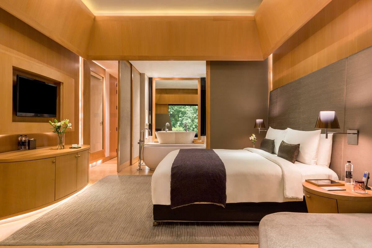 Ein modernes Hotelzimmer mit einem großen Bett, einem Schminktisch mit Spiegel, einem Fernseher und Blick ins Freie.