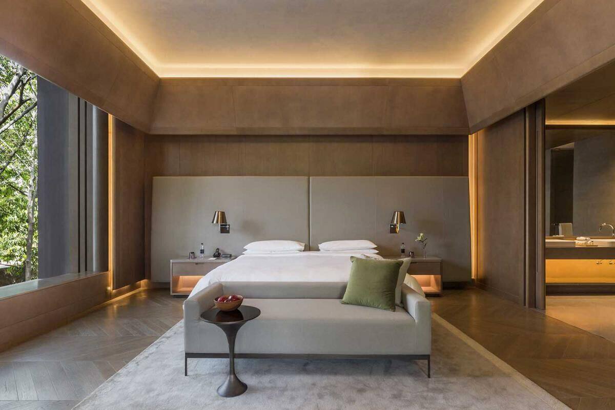 A modern hotel room with a large bed, bedside tables, a sofa, and a view of the outdoors.