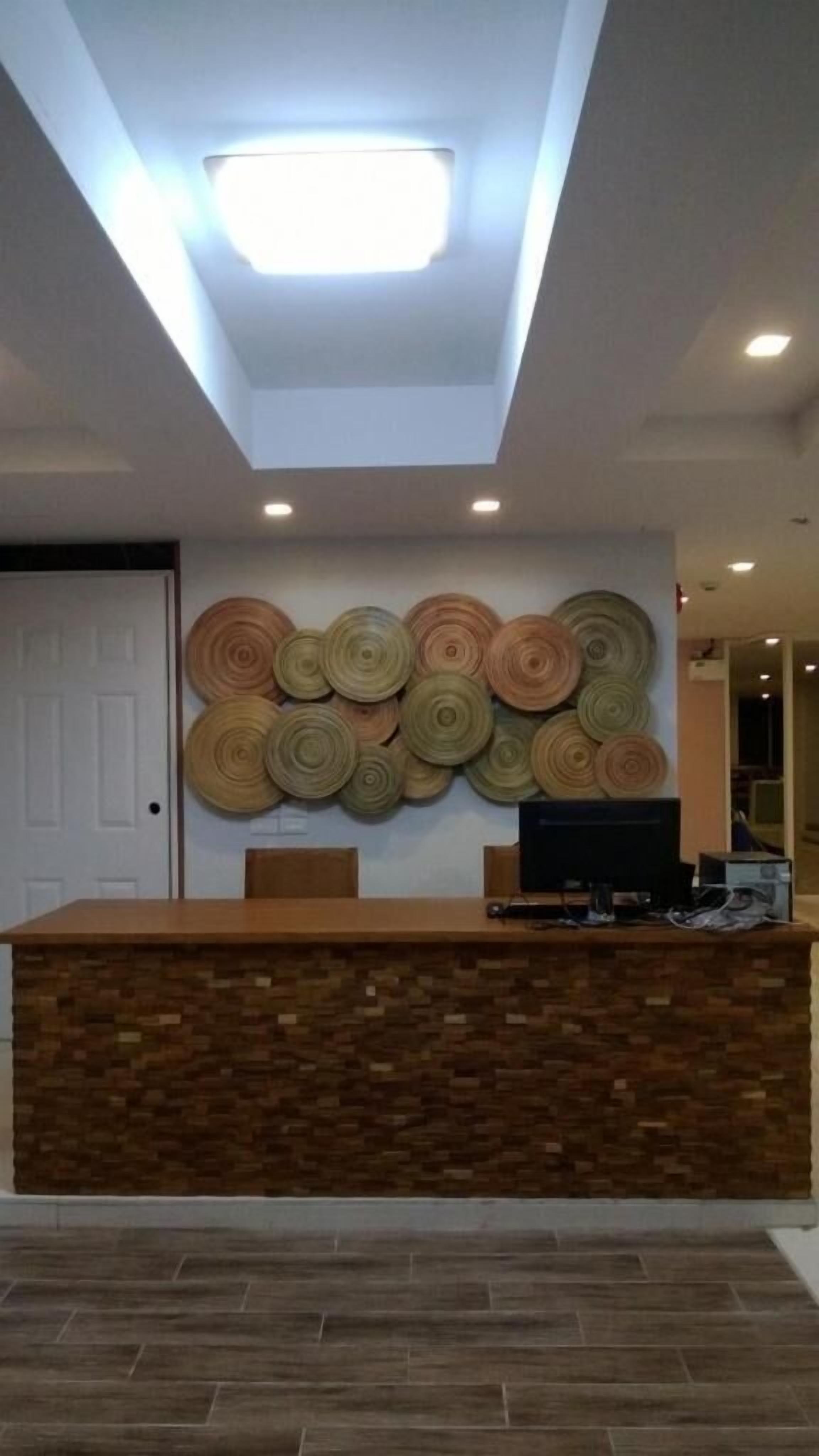 Un mostrador de recepción con detalles de madera y una base de piedra, una lámpara en el techo y una pared con elementos decorativos circulares.
