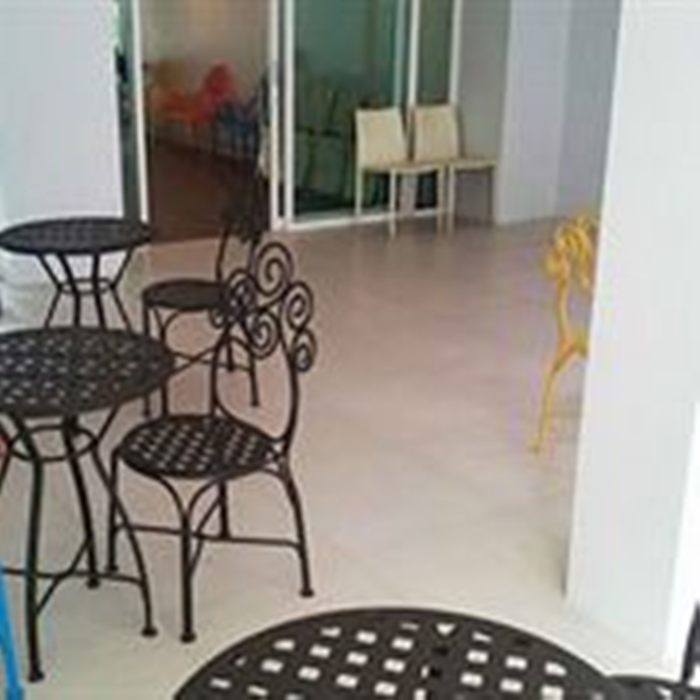 A small outdoor seating area with metal tables and chairs, a yellow decorative piece, and a view into the building.