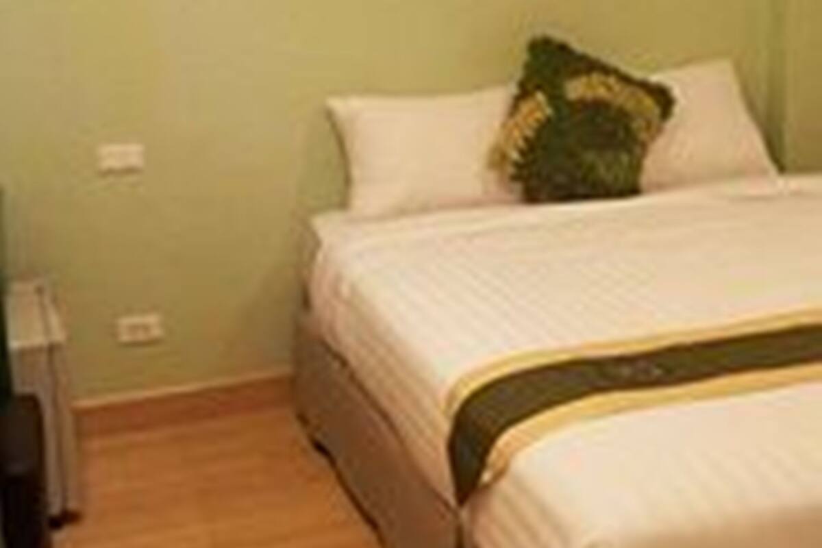 Quarto com uma cama, um travesseiro verde e um cobertor branco.