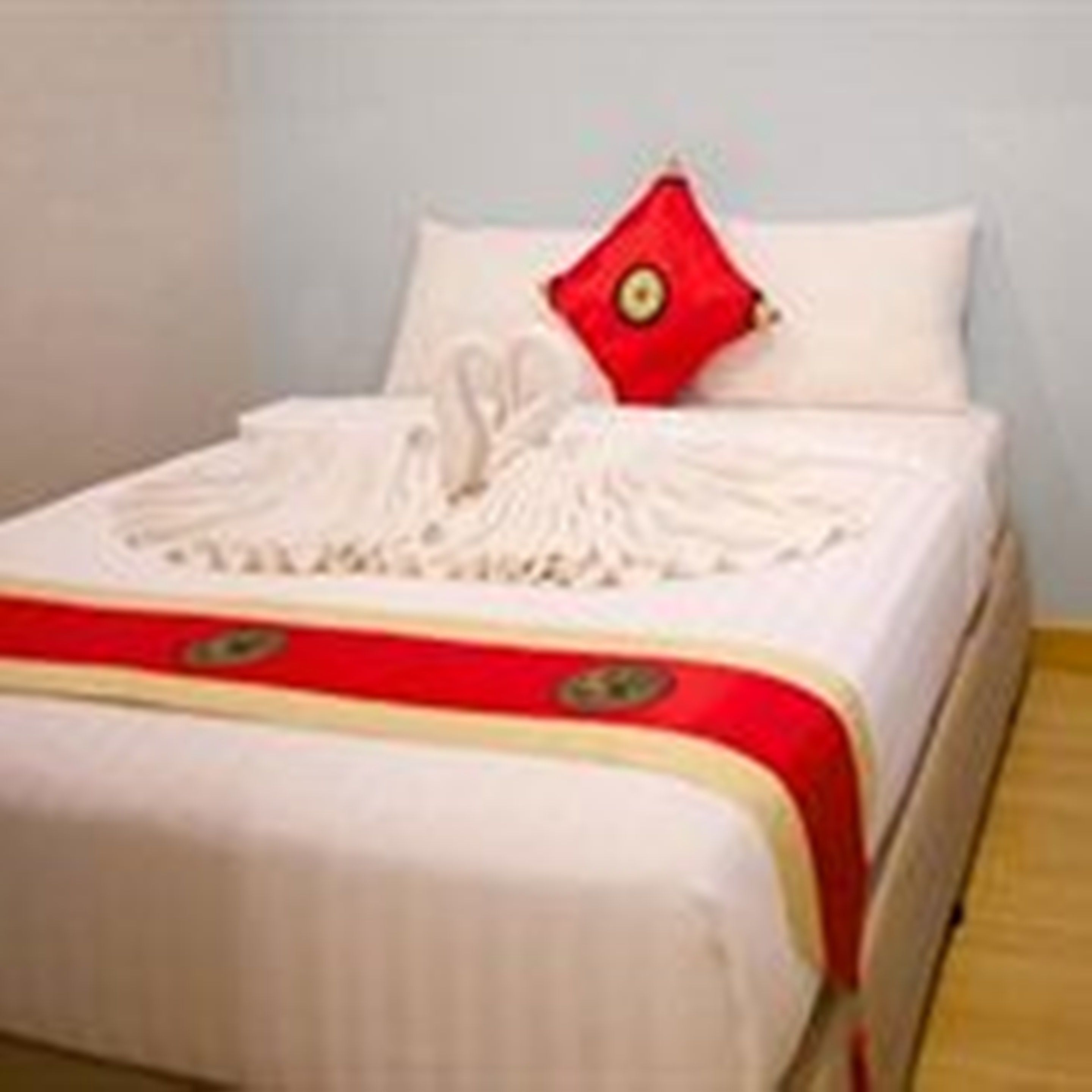 A neatly made bed with a white and red bedspread, a red pillow, and a white blanket.