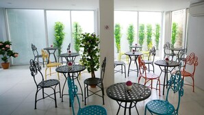 A spacious indoor area with multiple round tables and chairs, surrounded by large windows with greenery outside. - Nantra Chaweng Beach, Samui (Koh Samui)