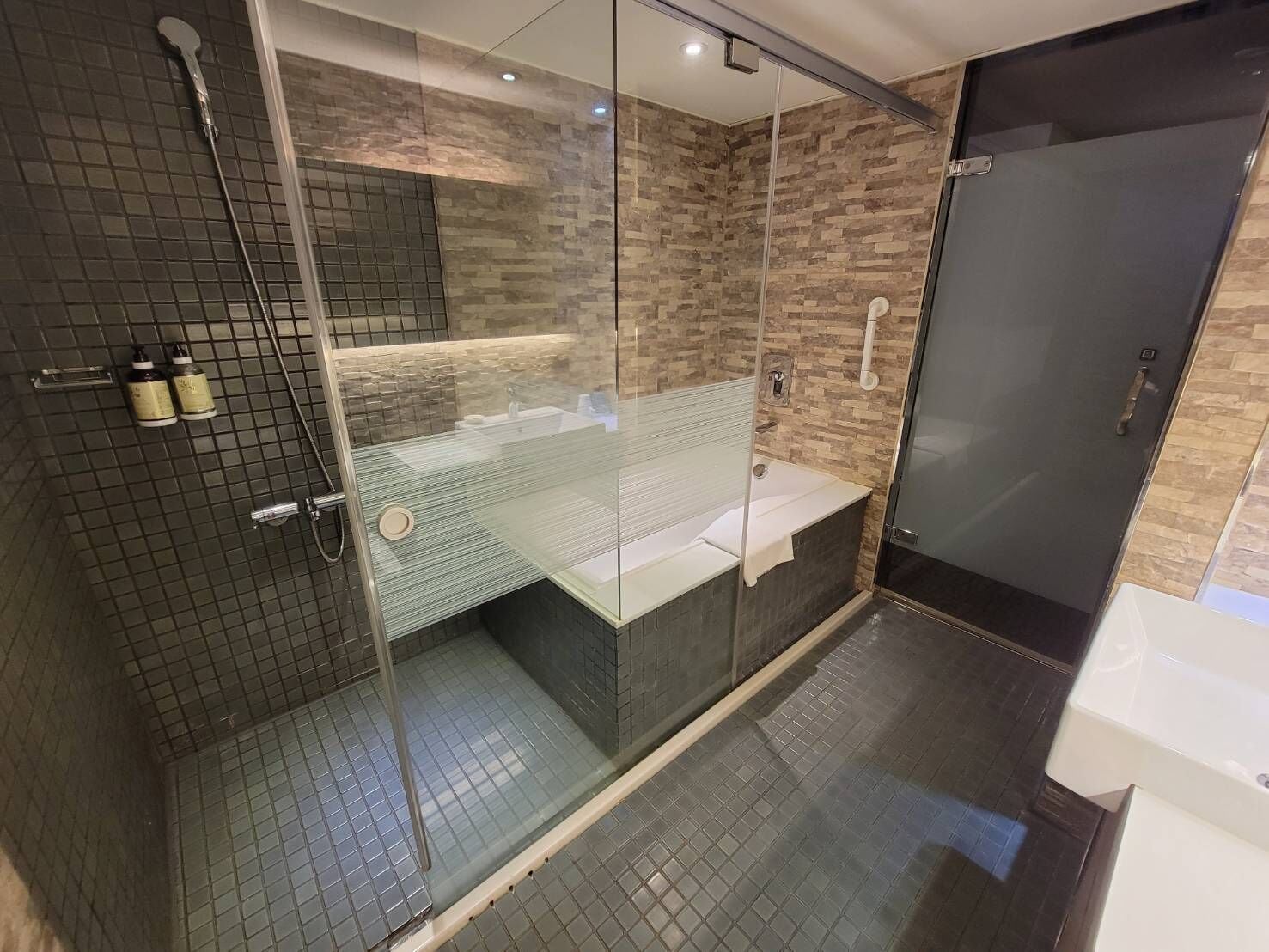 A modern bathroom with a glass-enclosed shower, a glass-topped vanity, and a dark tiled floor.