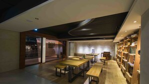 A modern interior with wooden tables and benches, a bookshelf, and a kitchen area. - Simple Plus Hotel (Taipei)
