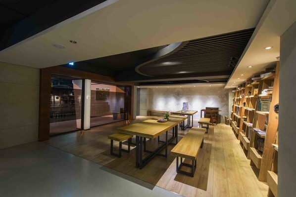 Een modern interieur met houten tafels en banken, een boekenkast en een keukenhoek.