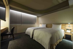 Een hotelkamer met twee bedden, een bureau, een stoel en een nachtkastje met een lamp.