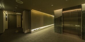 A modern hallway with a carpeted floor, a wall-mounted light strip, and an elevator with a metallic finish. - Simple Plus Hotel (Taipei)