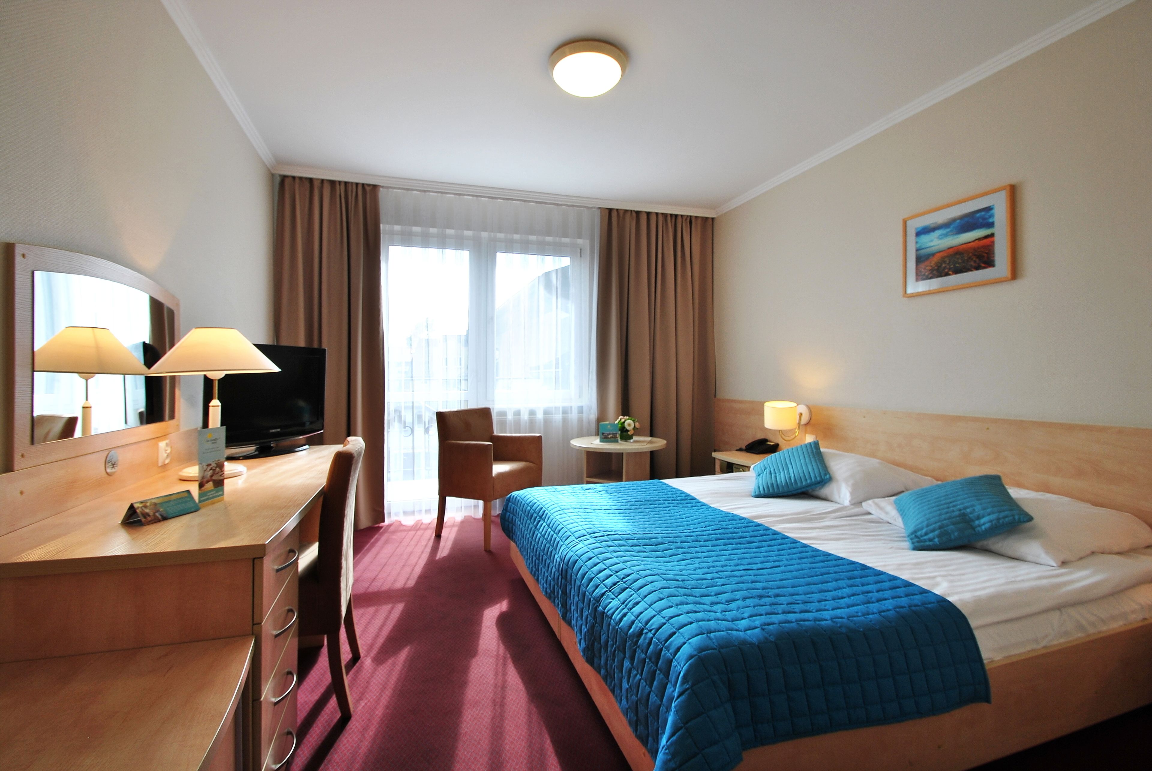 A hotel room with a bed, desk, chair, television, and a window with curtains.