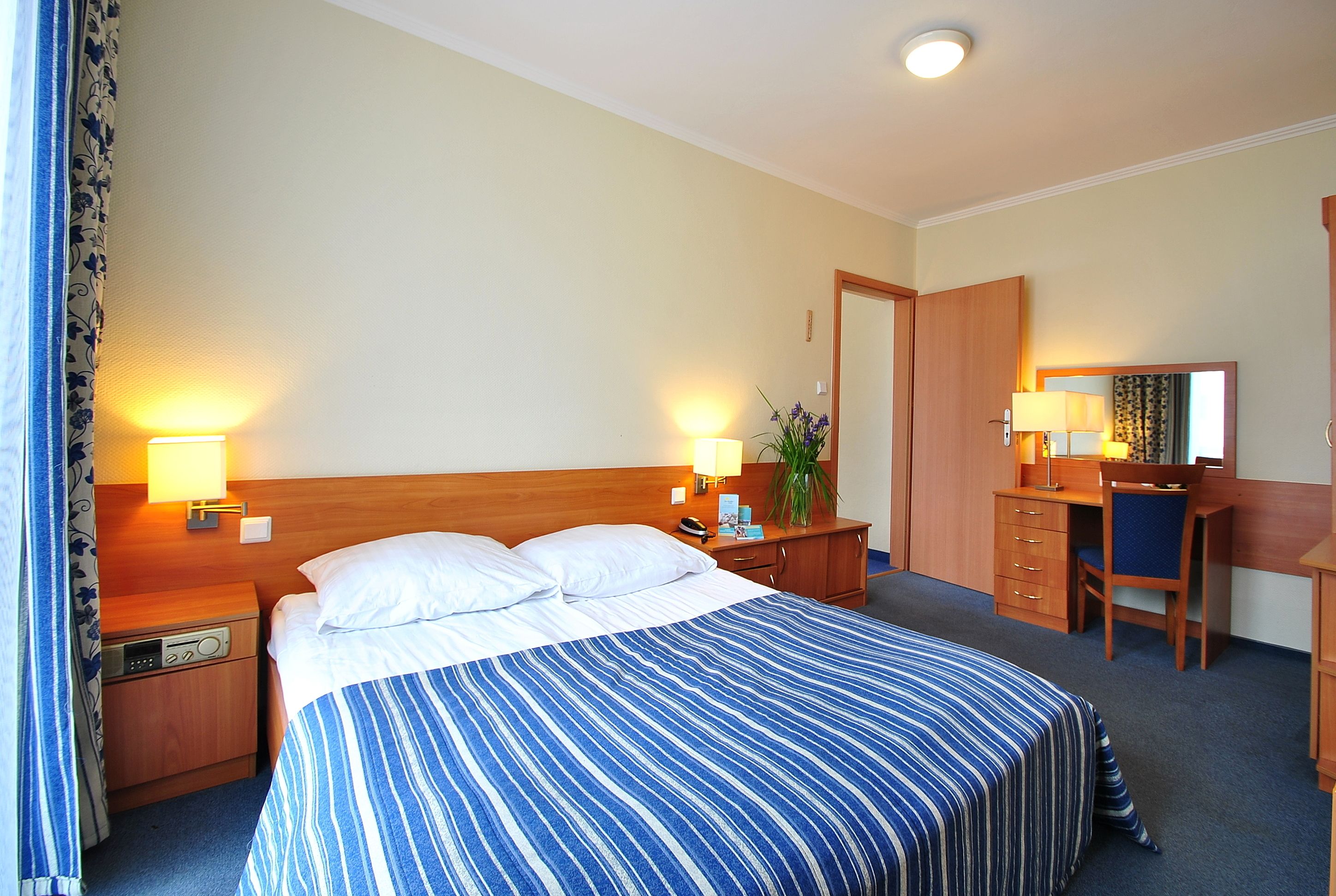 Una habitación de hotel con una cama, mesitas de noche, un escritorio, una silla y un espejo.