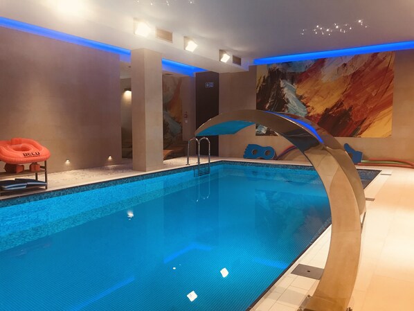 An indoor swimming pool with clear blue water, surrounded by beige walls and a modern design.