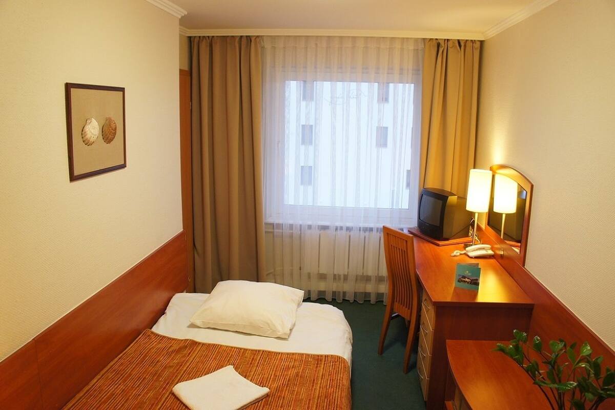 Une chambre d’hôtel avec un lit, un bureau équipé d’un ordinateur et d’une lampe, une chaise et une fenêtre avec des rideaux.