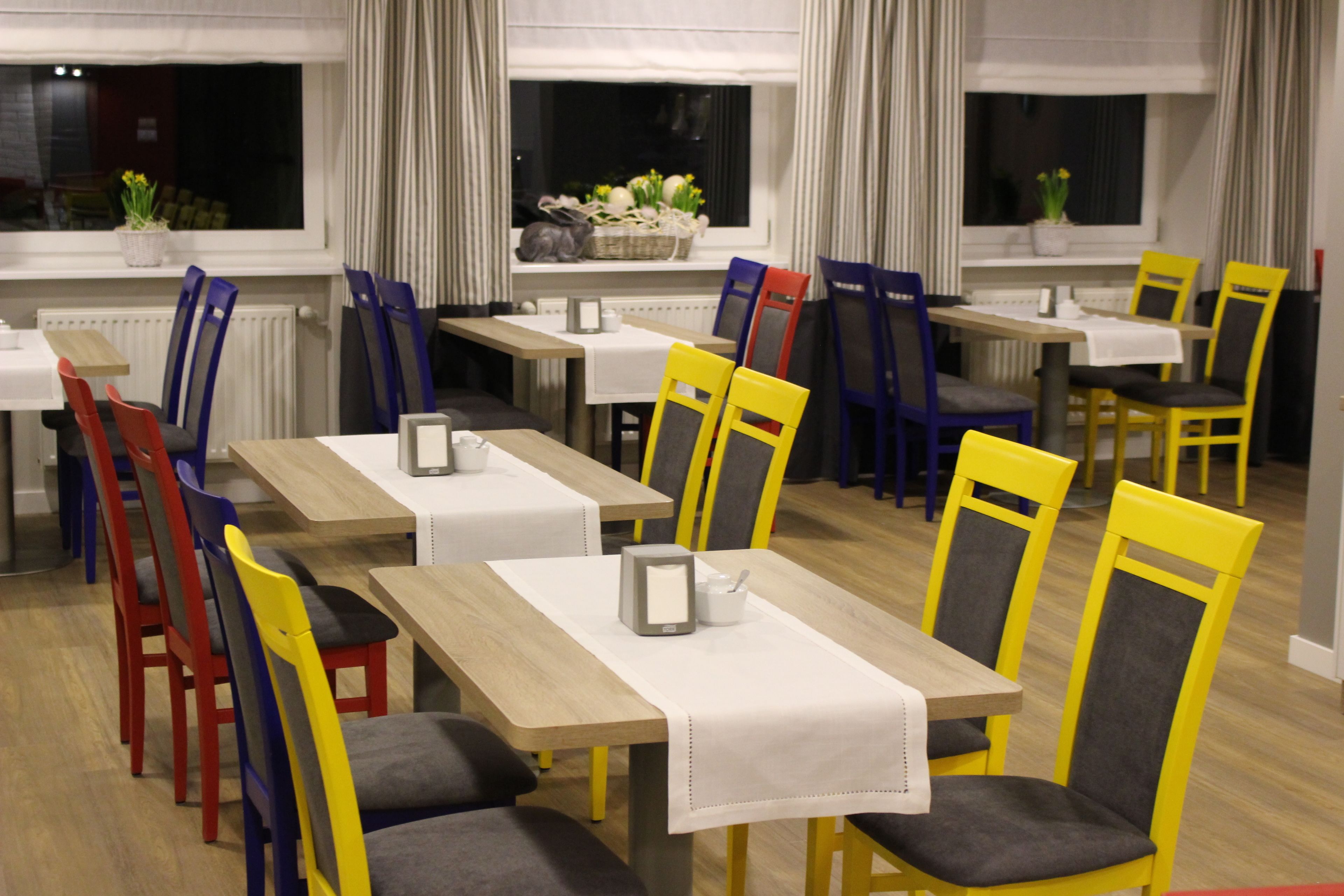 Un espace repas comprenant plusieurs tables et chaises, certaines recouvertes de nappes blanches et d’autres non.