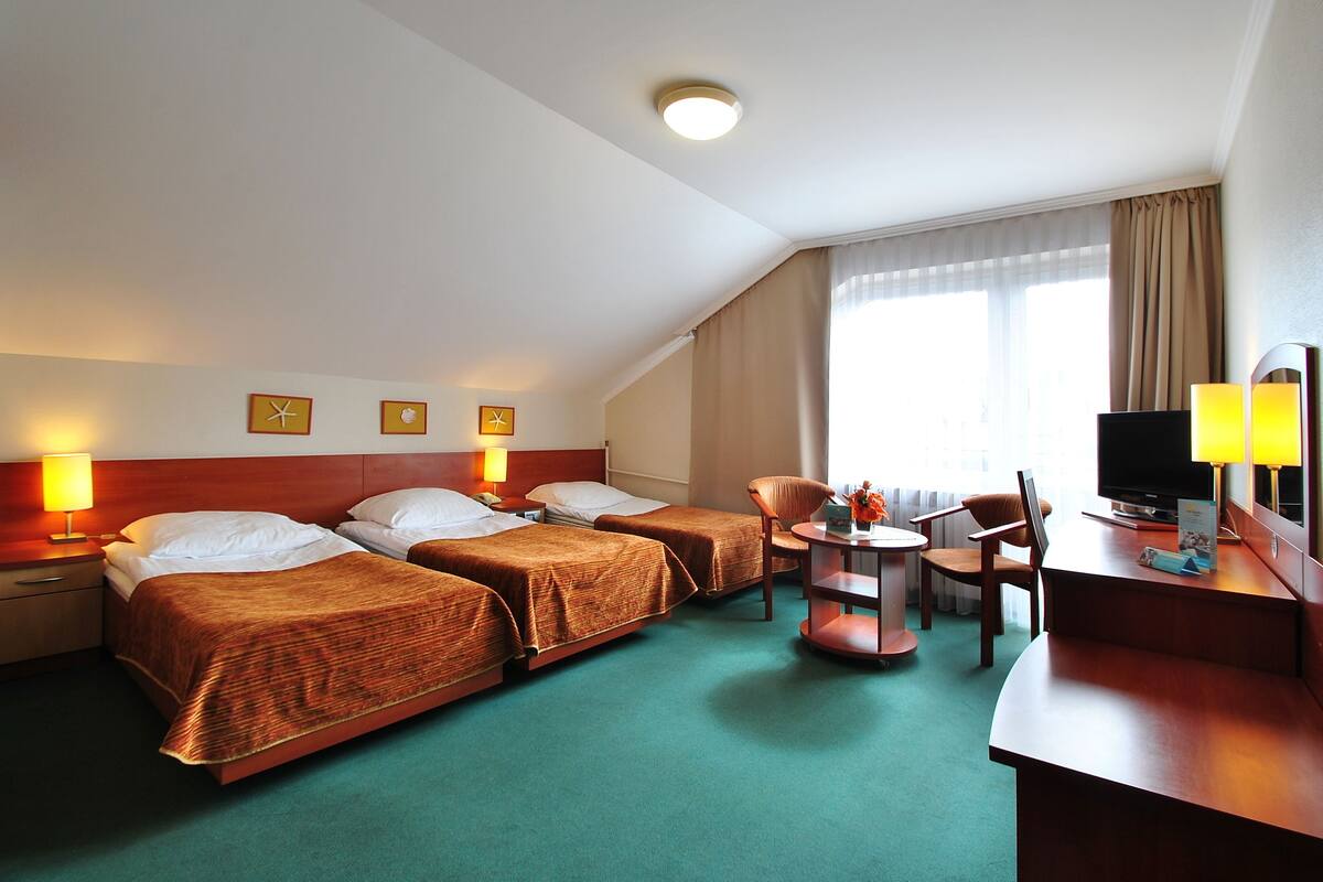 Une chambre d’hôtel avec deux lits simples, un bureau avec une chaise, une télévision et une petite table avec une lampe.