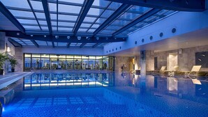 An indoor swimming pool with a glass ceiling, lounge chairs, and a view of the cityscape. - Expo Center Hotel  (Jinhua)