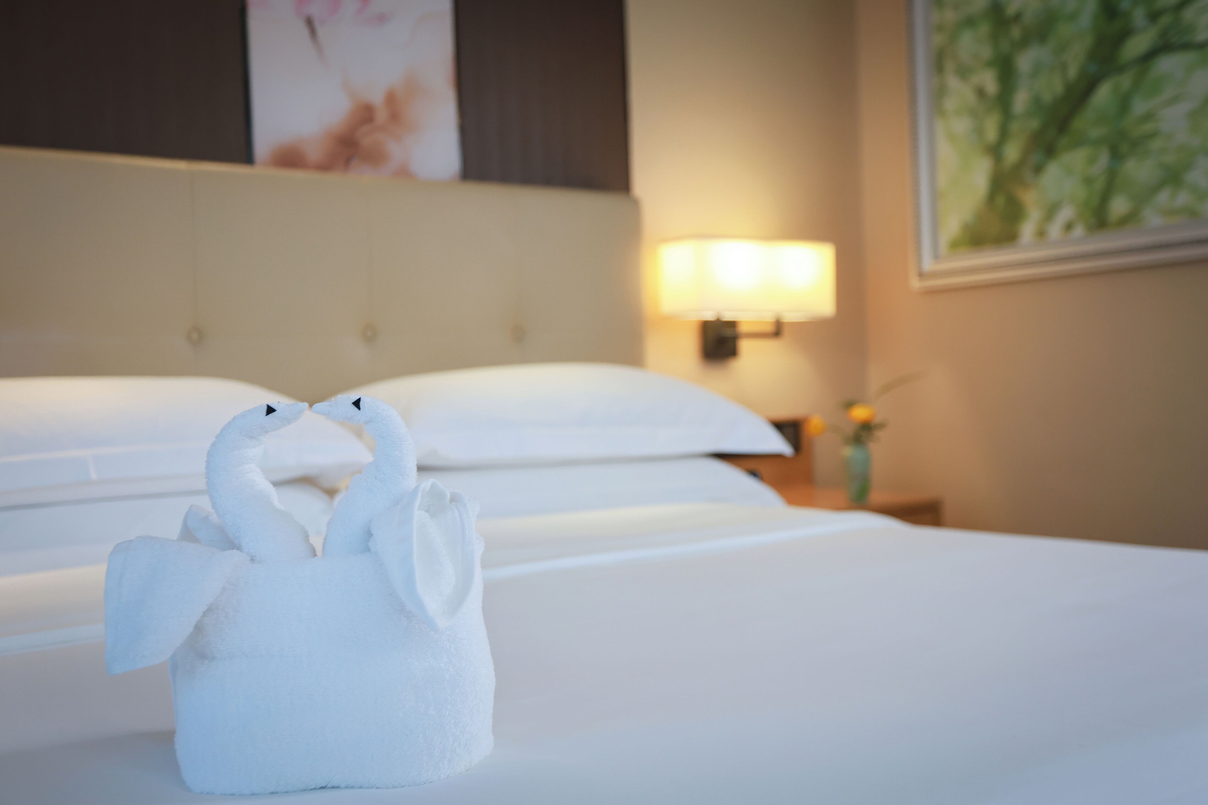 A hotel room with a bed, a wall-mounted lamp, and a painting.