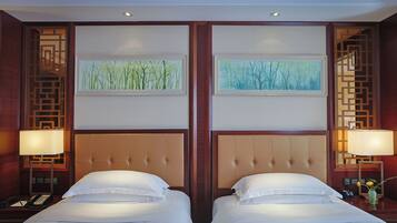 Habitación de hotel con dos camas, cada una con cabecero y mesita de noche con lámpara. En la pared, sobre las camas, hay cuadros enmarcados.