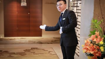 A man in a suit standing in a lobby with a wooden door and a floral arrangement.