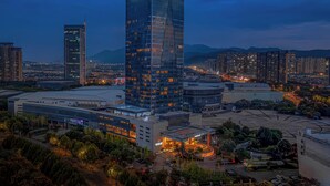 A high-rise hotel with a modern glass facade, surrounded by other buildings and a landscaped area with trees. - Expo Center Hotel  (Jinhua)